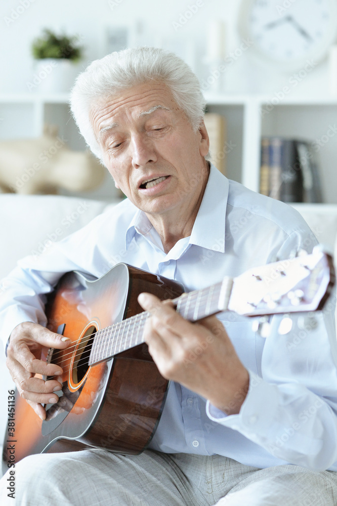Happy senior man with guitar sitting on the sofa at home Happy senior man with guitar sitting on the sofa at home