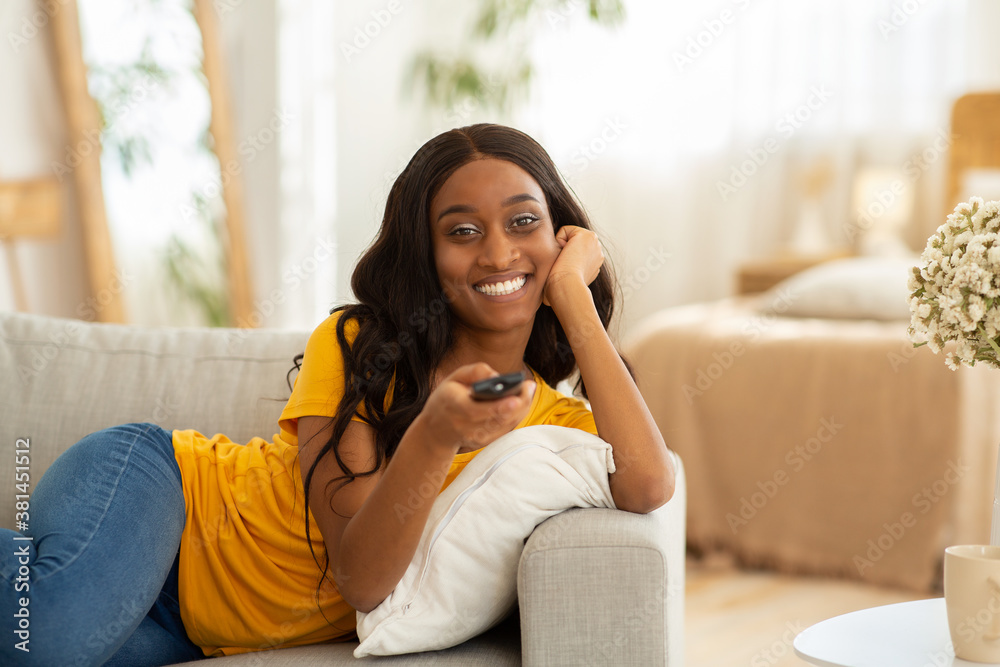 Weekend leisure activities. Millennial black woman with remote control switching channels on TV at home, copy space Weekend leisure activities. Millennial black woman with remote control switching channels on TV at home, copy space