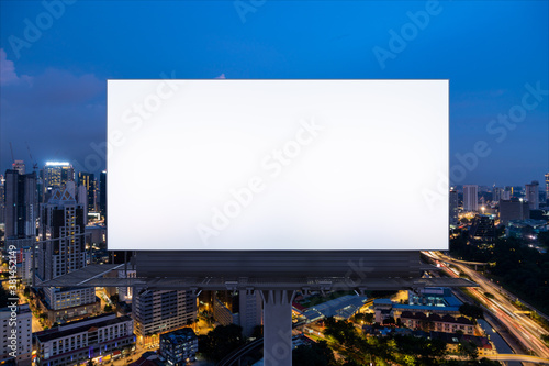 Blank white road billboard with KL cityscape background at night time. Street advertising poster, mock up, 3D rendering. Front view. The concept of marketing communication to promote or sell idea.