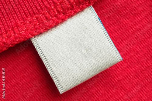 White blank laundry care clothes label on red cotton shirt background