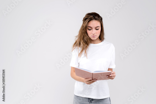 Pensive female writer ponders on new ideas, holds notebook has thoughtful expression, isolated over white background with copy space on the left