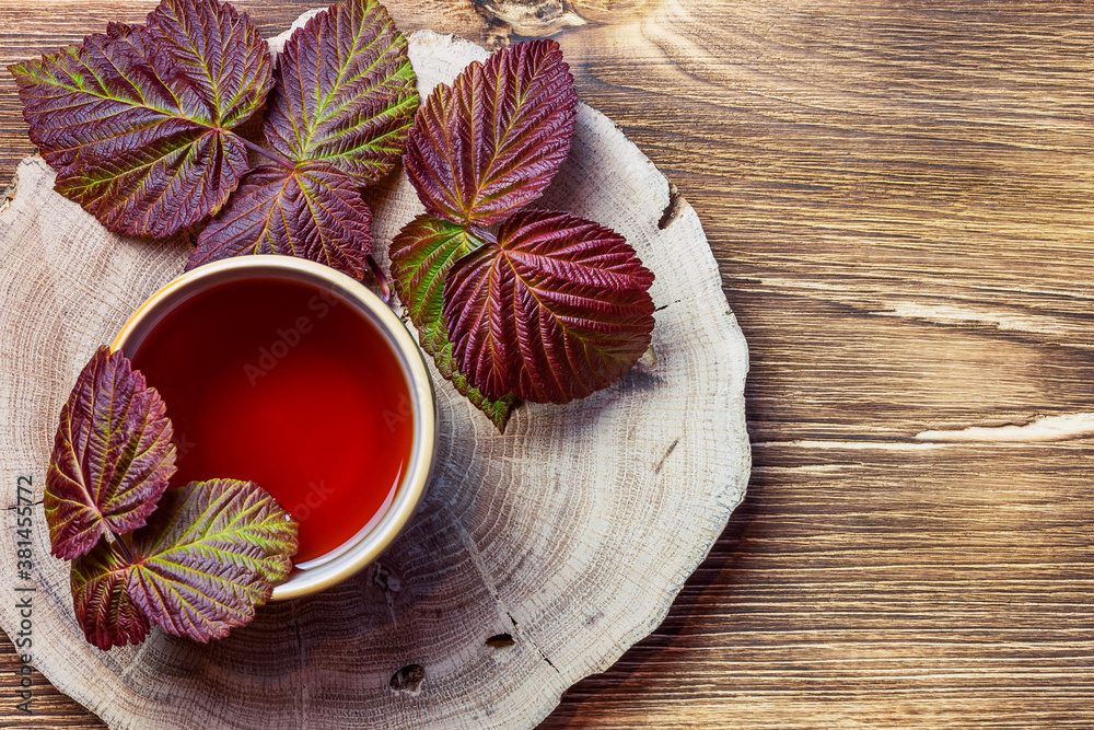 Morning evening relaxing warming medicinal aromatic tea from raspberry leaves in a cup anti-inflammatory antipyretic sedative, flat layout on natural wooden background Morning evening relaxing warming medicinal aromatic tea from raspberry leaves in a cup anti-inflammatory antipyretic sedative, flat layout on natural wooden background
