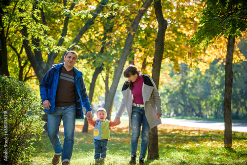 Beautiful young family on a walk in autumn forest on maple yellow trees background. Father and mother hold son on hands. Happy family leisure together concept