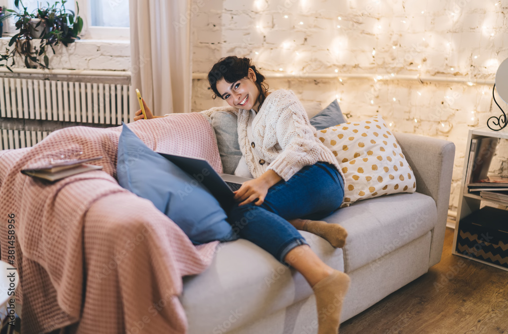 Obraz premium Cheerful woman resting on couch with laptop and smartphone