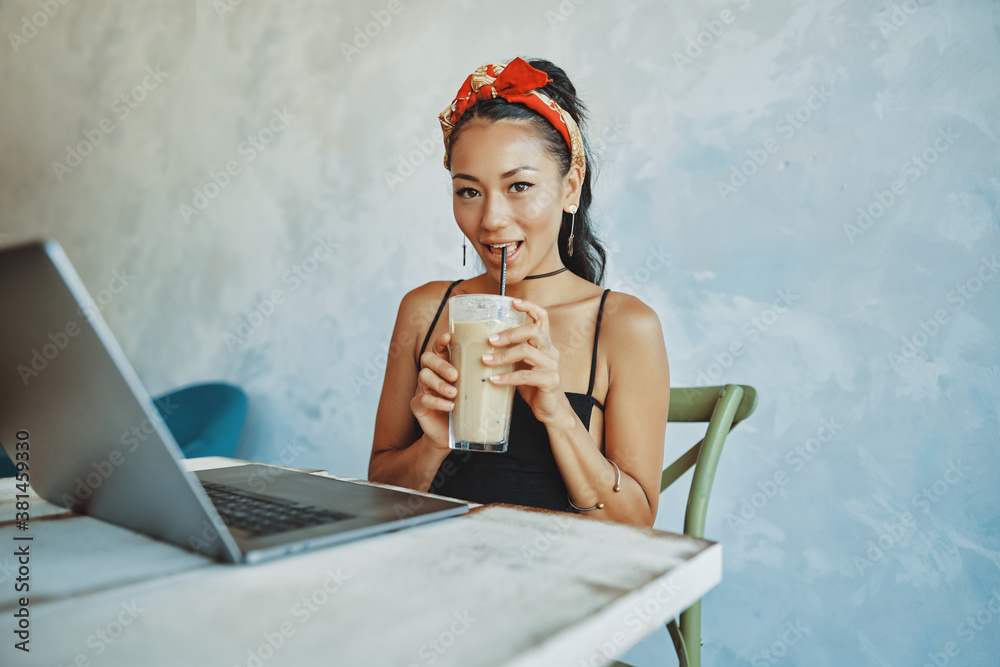 a young mixed race woman drink iced coffee and using her laptop in cafe