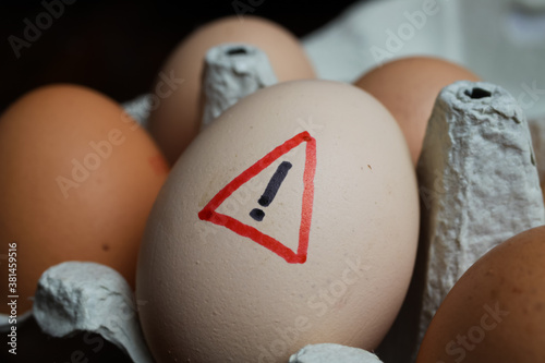 Foto Closeup of isolated raw brown eggs in carton box with warning sign - salmonella