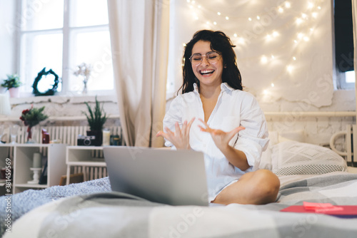Cheerful woman using laptop in decorated with lights bedroom