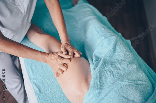 Young unrecognizable woman lying on massage table and enjoying therapeutic massage. Body care, losing weight concept. Hands masseur massage therapist doing anti-cellulite massage in spa clinic.