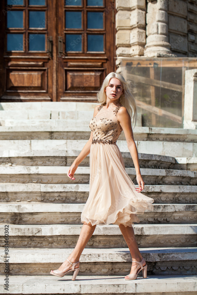 young beautiful girl in beige dress posing on the stone steps