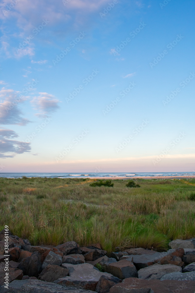 A Gorgeous View of Sand Dunes Covered in Plants With the Ocean and Sky Over Them at a Rock Wall