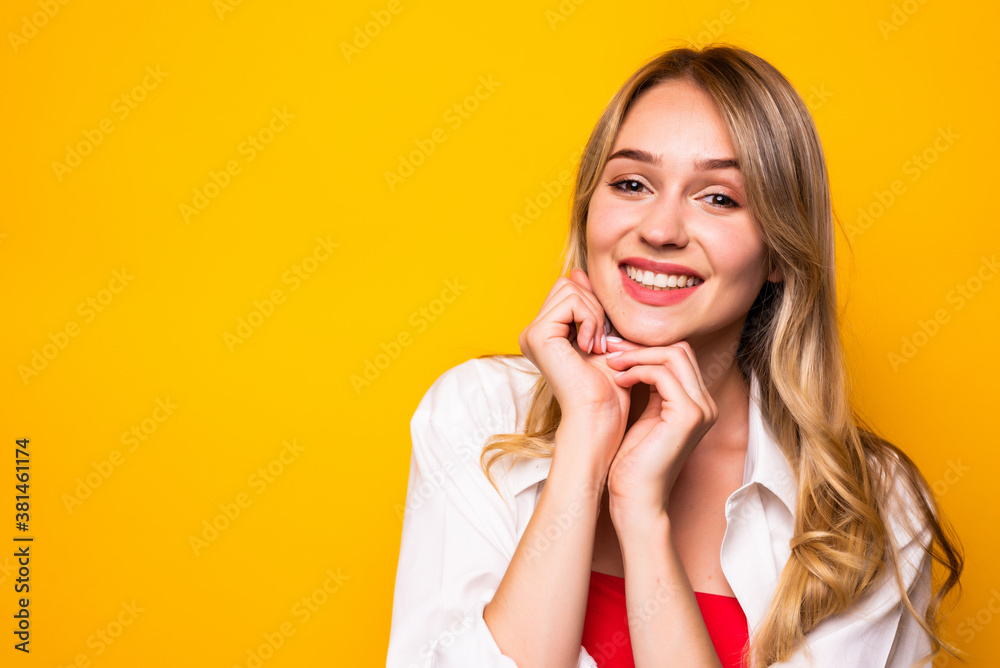 Beautiful young woman holding hand on chin, smiling, and looking at camera on yellow background. Beautiful young woman holding hand on chin, smiling, and looking at camera on yellow background.