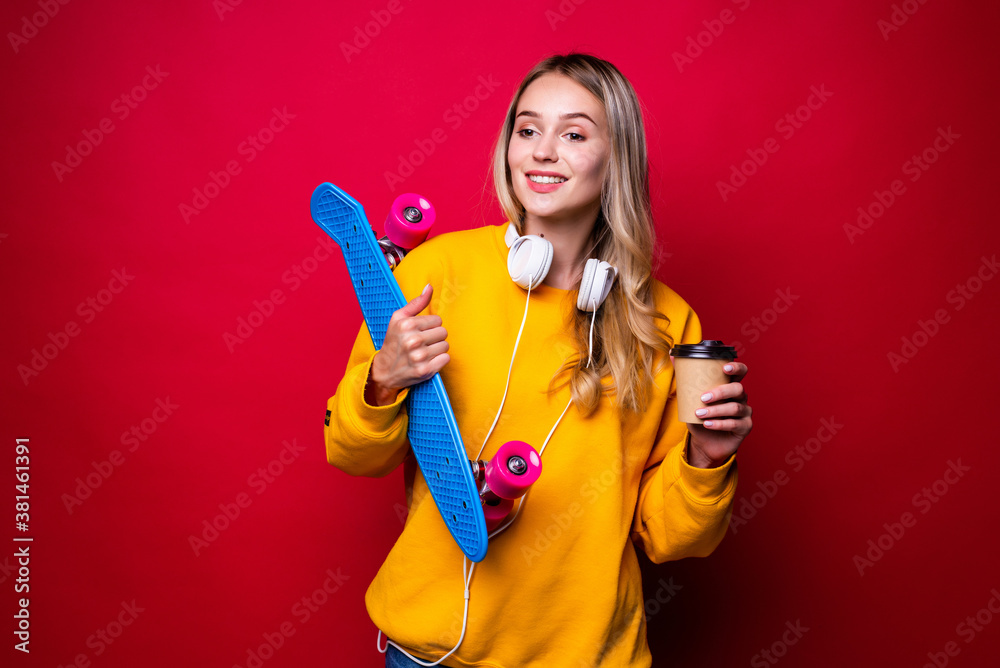 Young woman holding skateboard on shoulder and coffee against red background Young woman holding skateboard on shoulder and coffee against red background