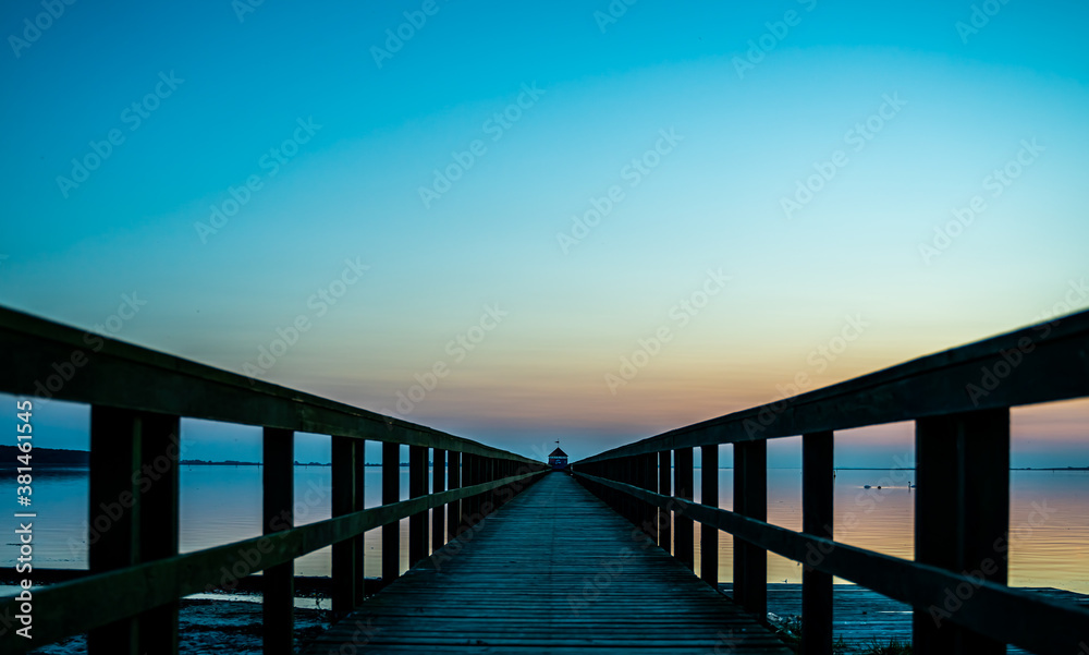 Wooden pier by the ocean at sunset, view down along the boardwalk.