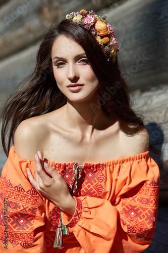 Beautiful Slavic woman in an orange ethnic dress and a wreath of flowers on her head. Beautiful natural makeup. Portrait of a Russian girl