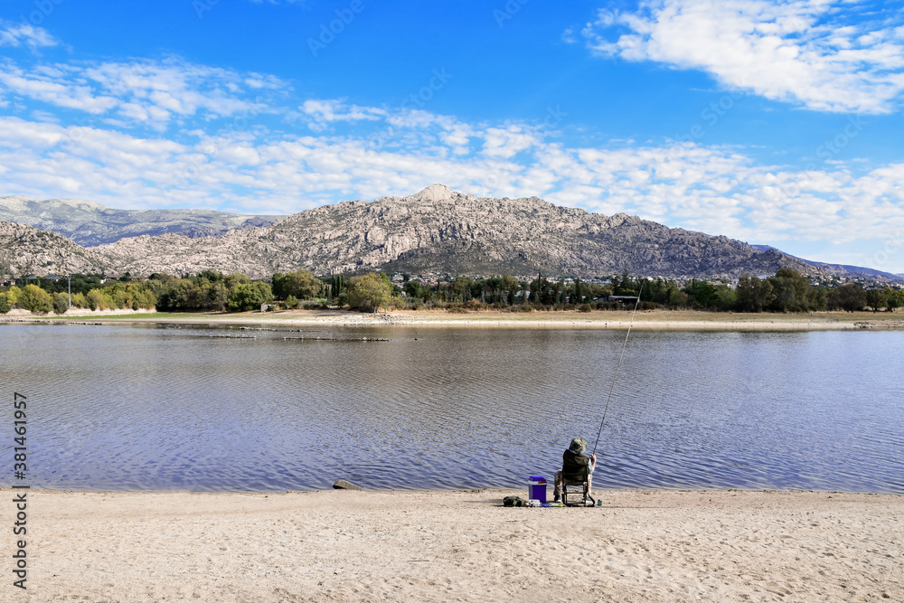 Fisherman angling in the lakeshore of the “Santillana” reservoir with the “Guadarrama” mountain range in the background