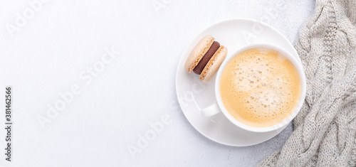 Horizontal banner with knitted scarf, coffee and chocolate macaron on stone background. Cozy autumn composition. Flat lay, top view