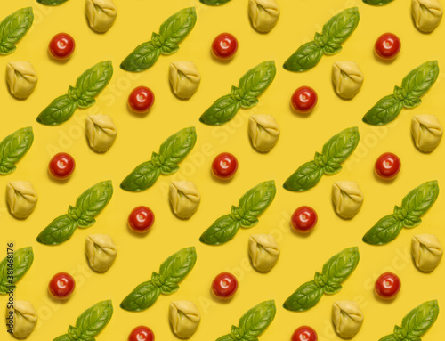 Many tortellini with basil and cherry tomatoes on yellow background. Italian food pattern