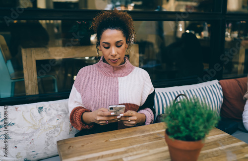 Thoughtful young ethnic lady with smartphone in cozy cafe