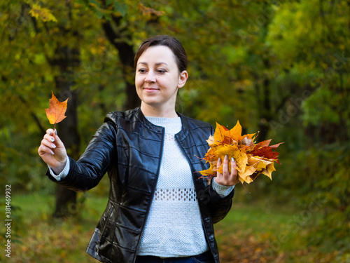 a young woman in a leather jacket collects colorful leaves in an autumn Park. bright and beautiful autumn. nature walk.