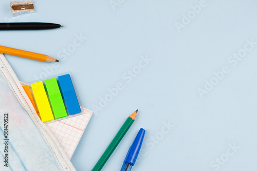 School supplies with a mask on a blue background. View from above. Place for text. Epidemic. Education concept.