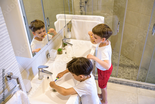 Older brother learning to clean the teeth for younger brother in the bathroom with mirror