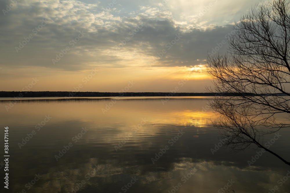 Moody evening lake landscape with sunset over water edge and sky reflecting in the water.