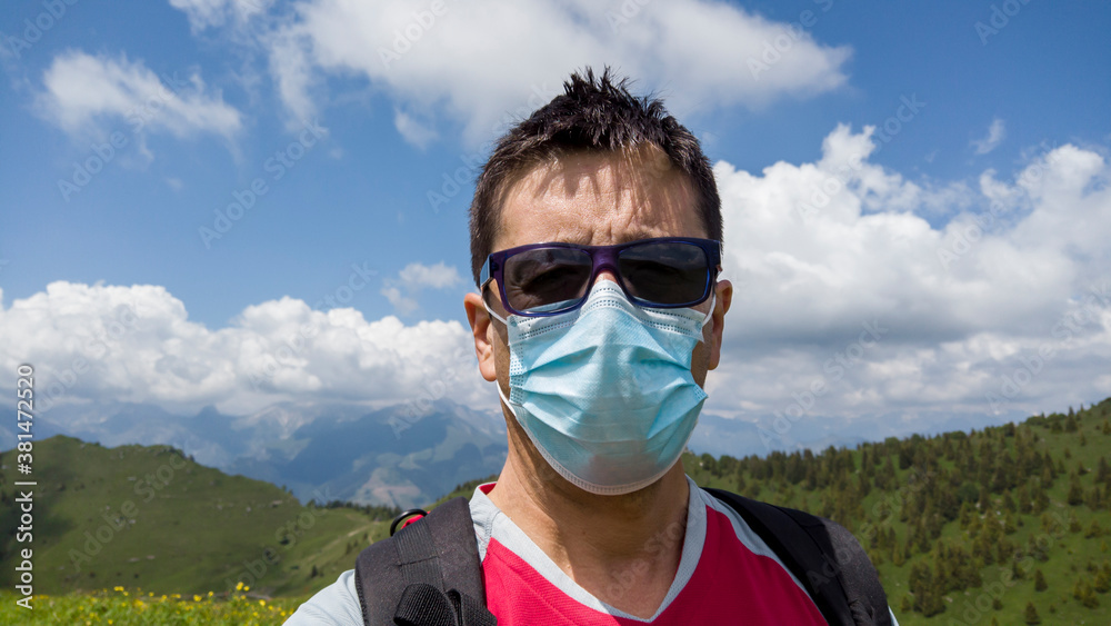 Close up of middle aged man with surgical mask and sunglasses. Background with mountains. Use of the mask during outdoor. Summer contest. Mountain hiking