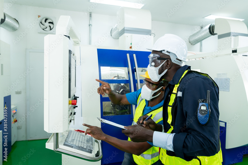 Professional engineer wearing a hard hat and safety glasses operating CNC milling machine in manufacturing workshop. Male worker working on a lathe machine in metal industry factory on business day. Professional engineer wearing a hard hat and safety glasses operating CNC milling machine in manufacturing workshop. Male worker working on a lathe machine in metal industry factory on business day.