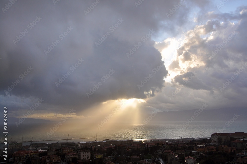 Dramatic blue sky with sun whose rays pierce the cloud and reflect to the sea

