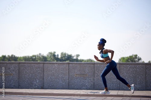 side view on young black woman running, develops endurance before marathon