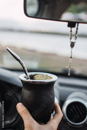 joven tomando bebida tipica argentina llamada mate, en el auto en un día nublado frente al río