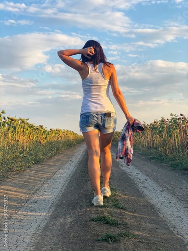 Young girl in shorts and white T-shirt is walking along country road photo