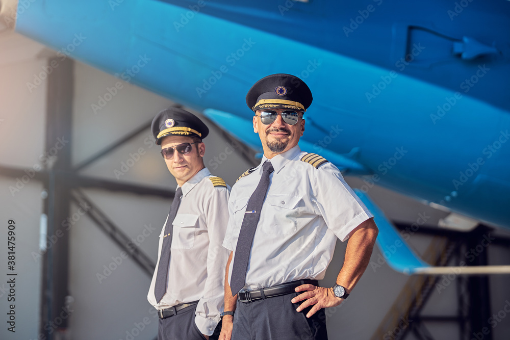Happy smiling men in sunglasses standing in the hangar at the airport Happy smiling men in sunglasses standing in the hangar at the airport