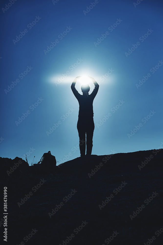 Dark silhouette of a young girl traveler on the top of the mountain indulge and rejoice against the background of the sun