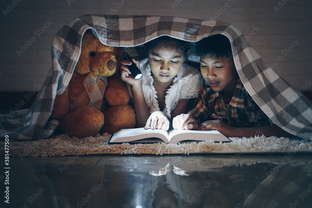 Happy children boy and girl reading a book in blanket at home with a toy teddy bear. - obrazy, fototapety, plakaty 