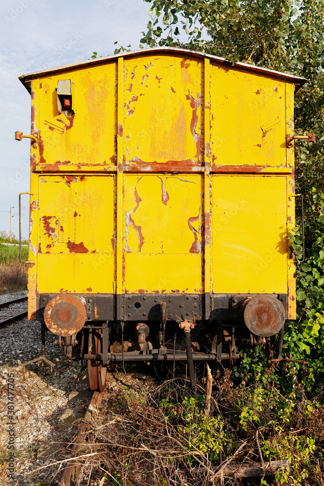 Back view of an old yellow train, abandoned and rusty, on an old tracks in the nature