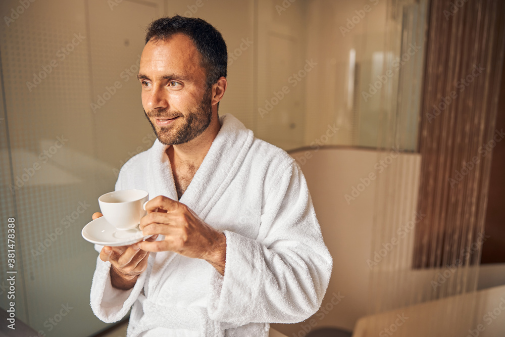 Joyful young man drinking coffee in spa salon Joyful young man drinking coffee in spa salon