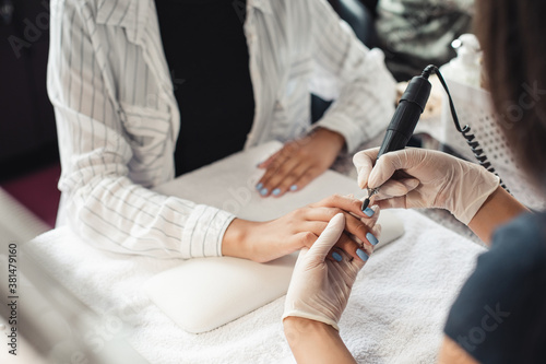 Beauty day and nail treatments. Professional manicure master in rubber gloves makes procedure removes varnish with an electric manicure device to african american client