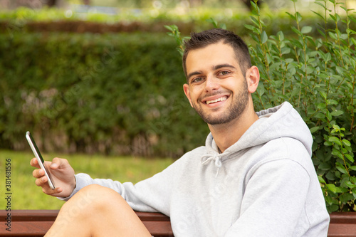 attractive young man with beard and mobile phone sitting in the park