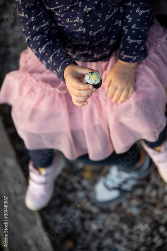 The little girl holds her hands and eats sushi.