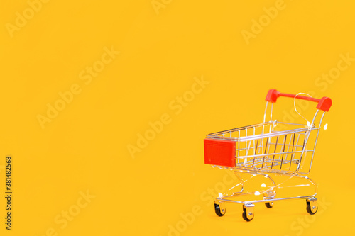 Toy shopping cart on a yellow background. Copy space. The concept of shopping and consumerism