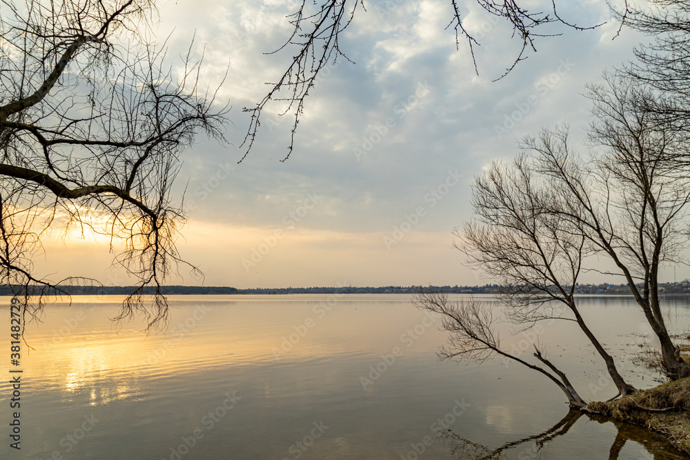 Moody evening lake landscape with sunset over water edge and sky reflecting in the water.