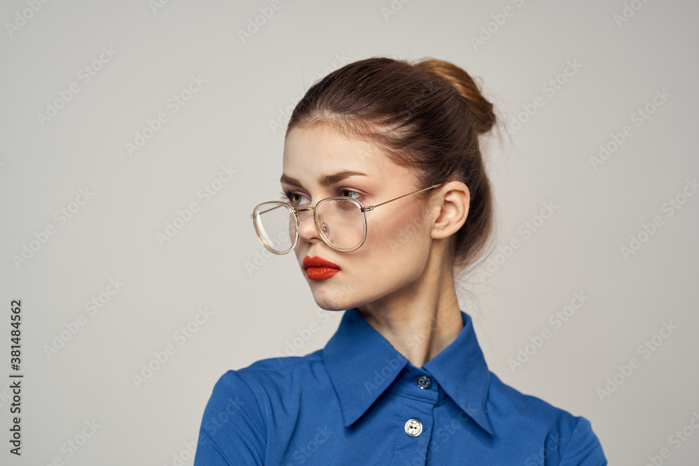 Strict woman in glasses and in a blue shirt on a light background portrait cropped view