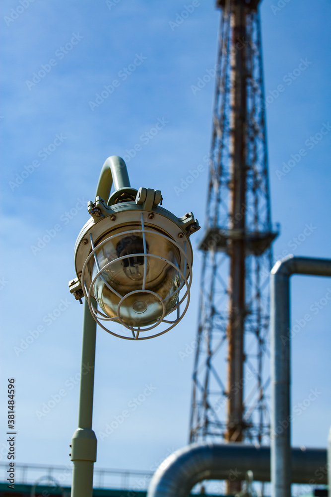 Petrochemical plant. Explosion-proof lamp on oil refinery plant. Focus on foreground. The girder tower blurred. Blue sky background.