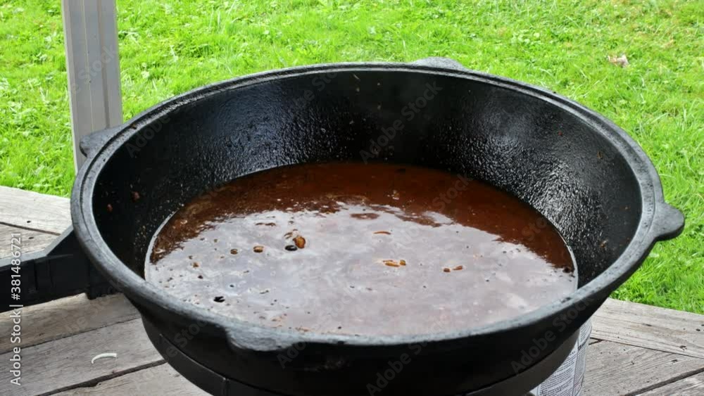 Cooking real Uzbek pilaf during a cook stirs meat with iron spoon that stewed in the cauldron on of fire Cooking real Uzbek pilaf during a cook stirs meat with iron spoon that stewed in the cauldron on of fire