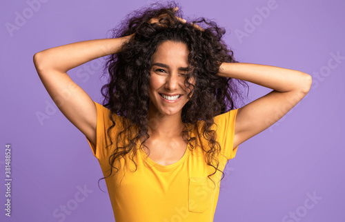 Portrait of beautiful brunette woman touching her natural curly hair and winking