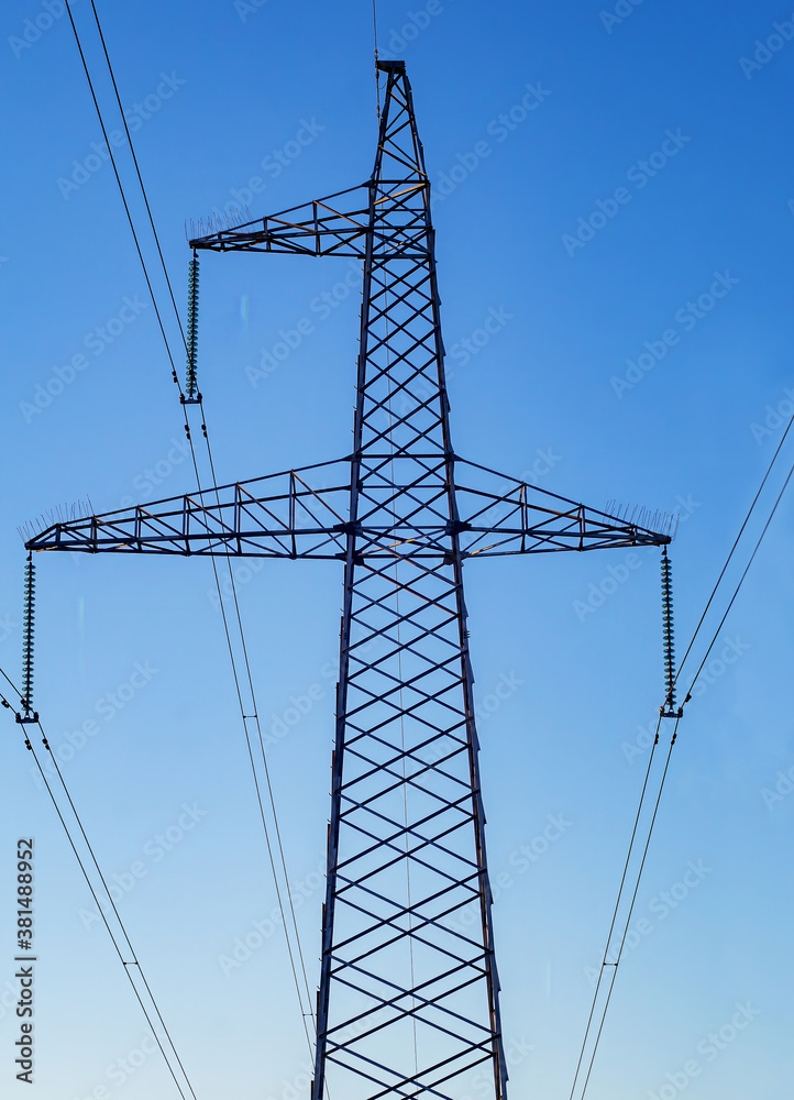 Metal support for power transmission lines 110/35/10 kV with wires and insulators against a blue sky. Electrical infrastructure system.