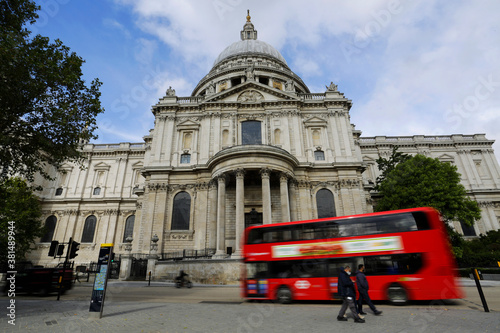 A double decker bus cross a street in front of the famous St. Paul's cathedral in central London, United Kingdom, during a sunny day.