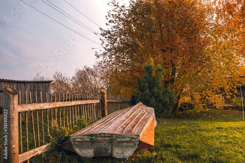 Tranquil rural landscape with a wooden fence, an old upturned boat, and autumn trees.