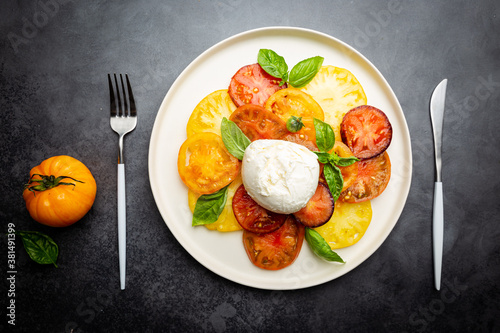 Delicious caprese salad with ripe colorful tomatoes and mozzarella cheese with fresh basil leaves. Italian food, top view